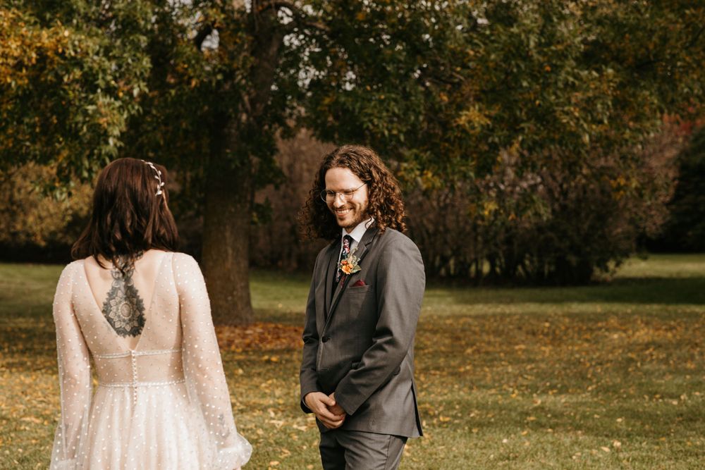 Groom smiles joyfully at bride in long-sleeve lace wedding gown during fall first look.