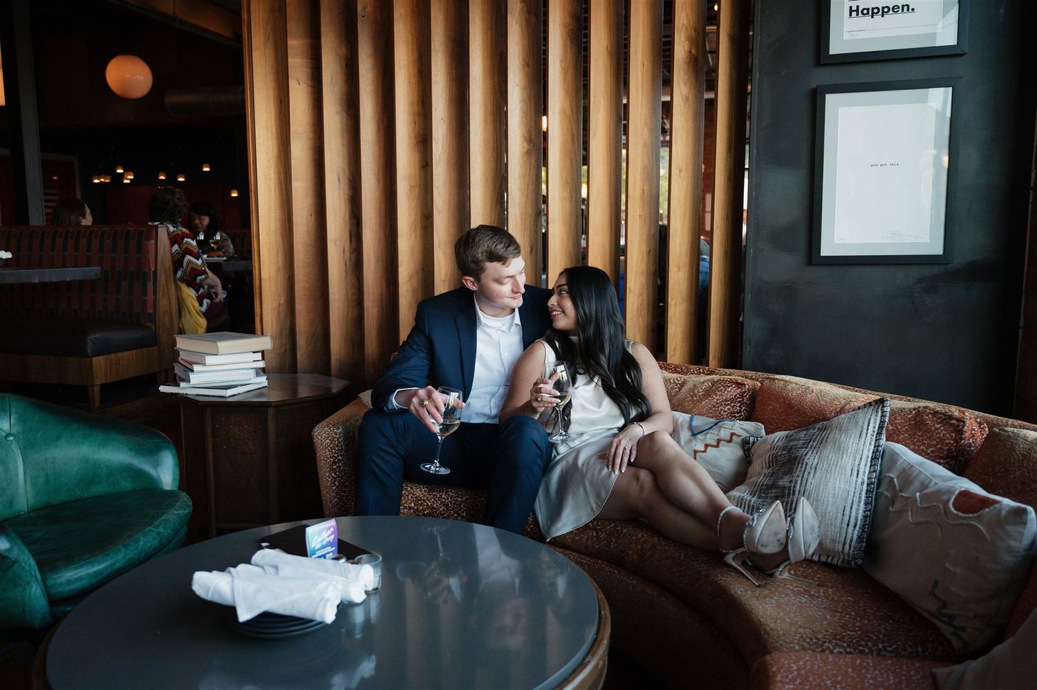 Stylish couple lounging on brown couch sharing drinks in modern restaurant setting.