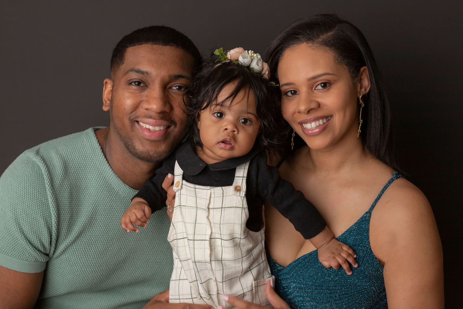 Warm family portrait with parents and baby against dark studio background.