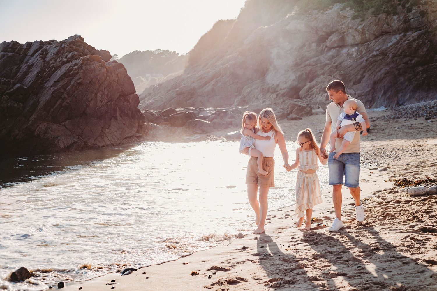 Family walking together along a scenic rocky beach at sunset.