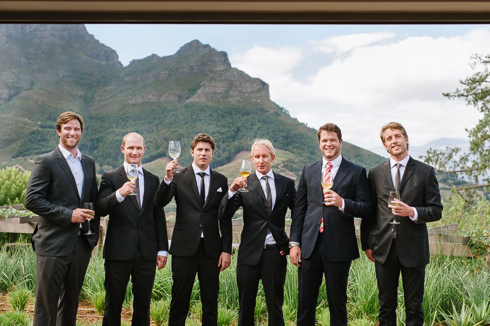 A group in matching dark suits poses outdoors with dramatic mountain peaks in the background.