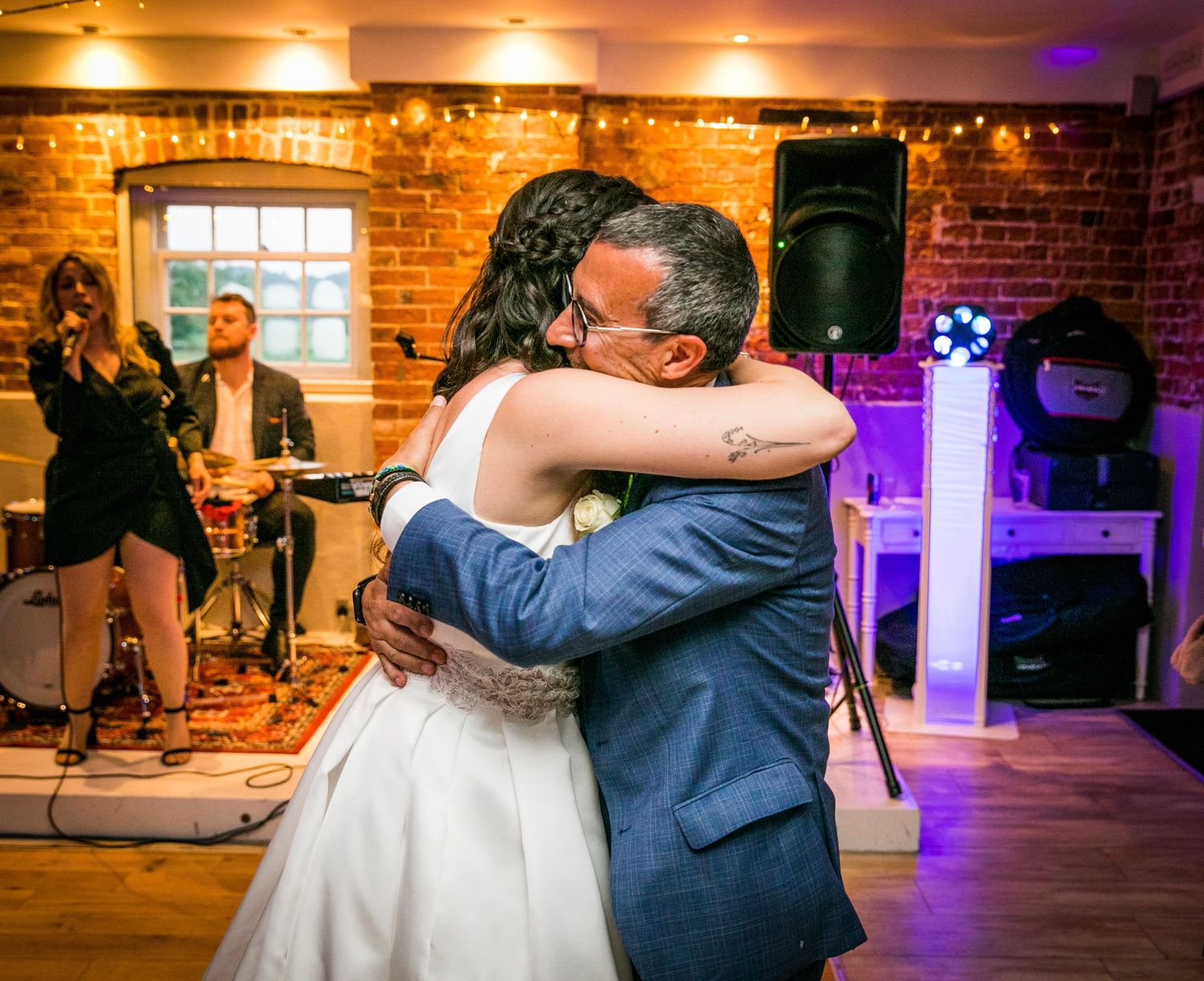 Couple shares romantic dance moves in a warmly lit brick venue with purple accent lighting.