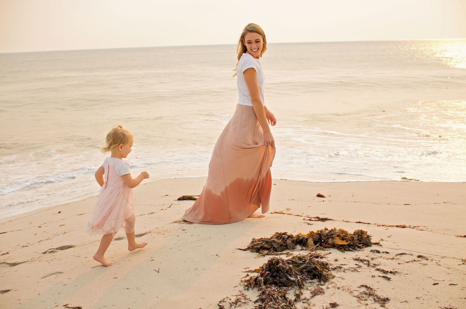 baby girl running after mum on beach smiling