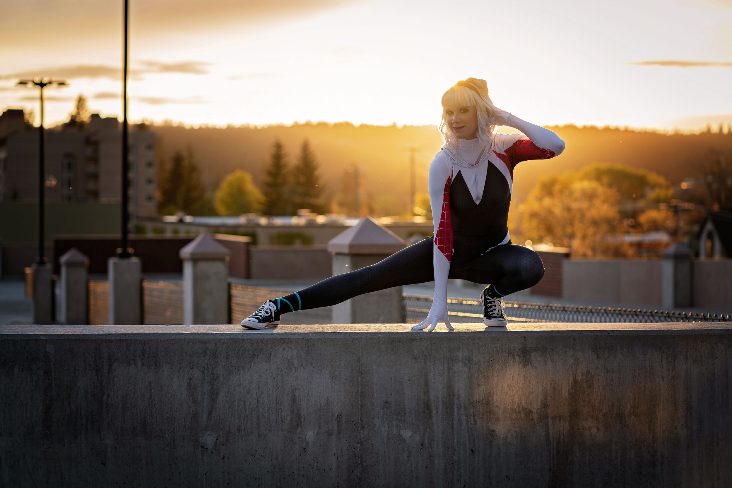 Athletic figure performs splits on concrete ledge during golden sunset.