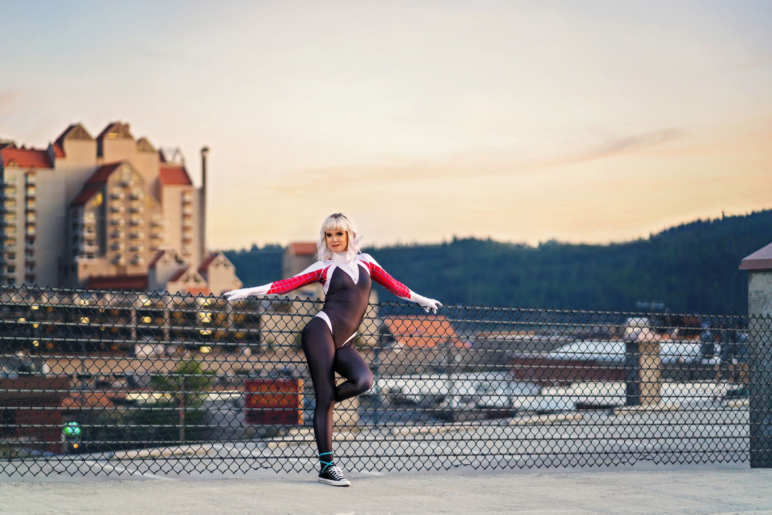 Dancer performs standing split pose on urban rooftop at sunset.