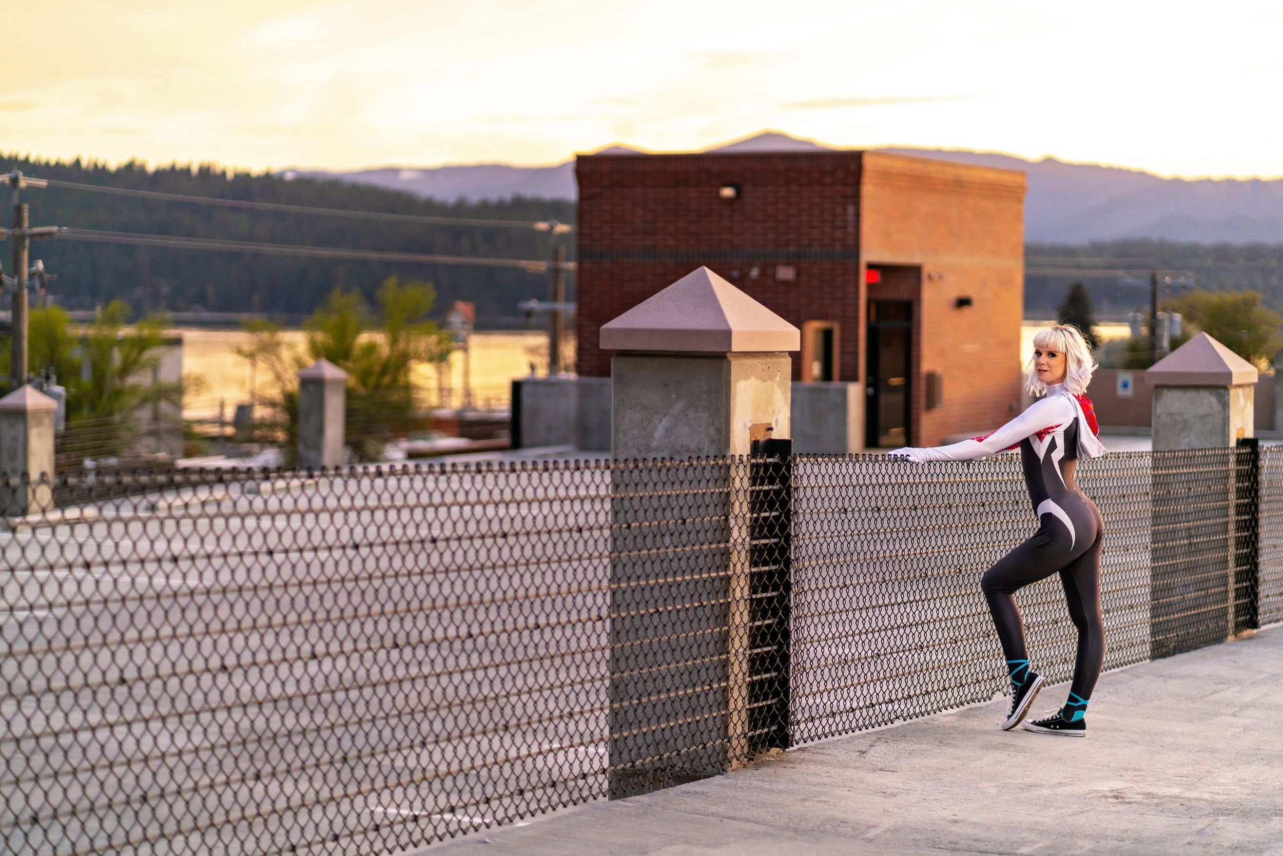 Athletic figure demonstrates balance pose on chain link fence at dusk.