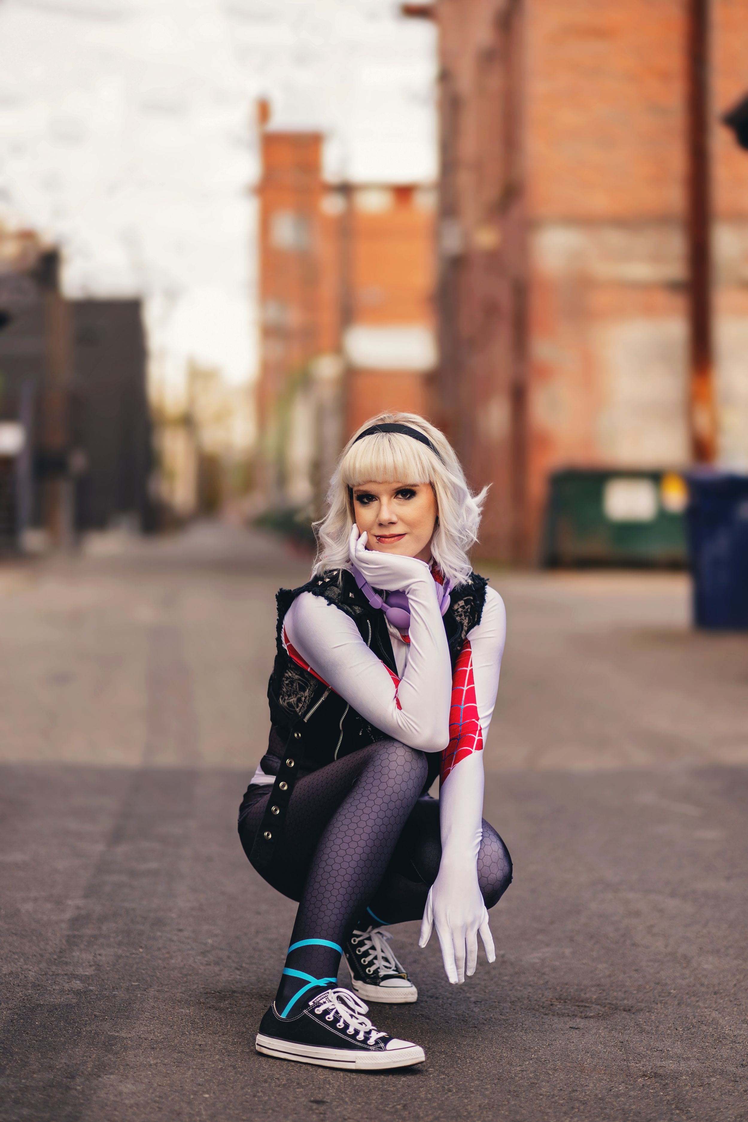 Figure in athletic wear crouches on urban street wearing sneakers and purple tights.
