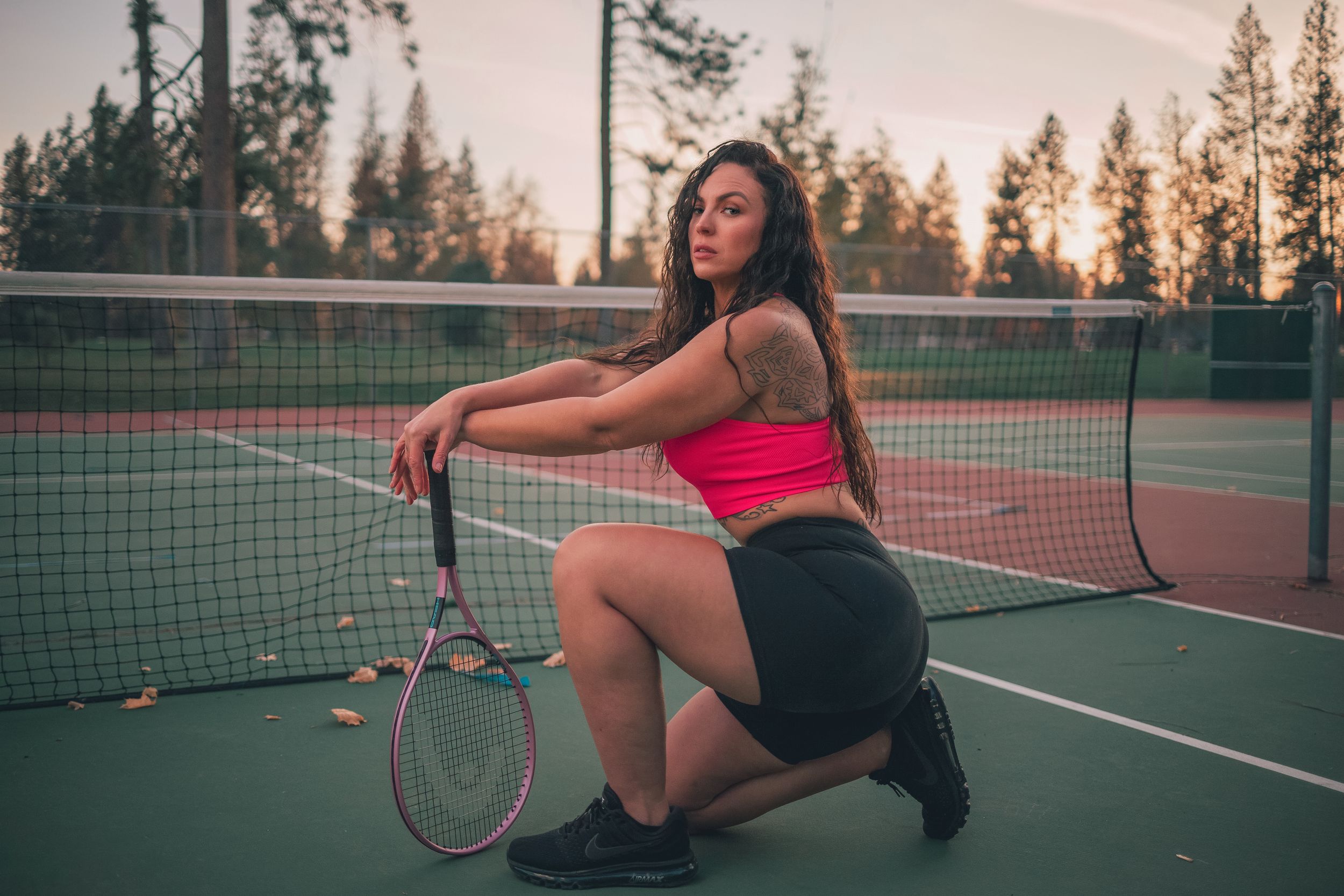 Sporty figure poses with tennis racket on court during golden hour.