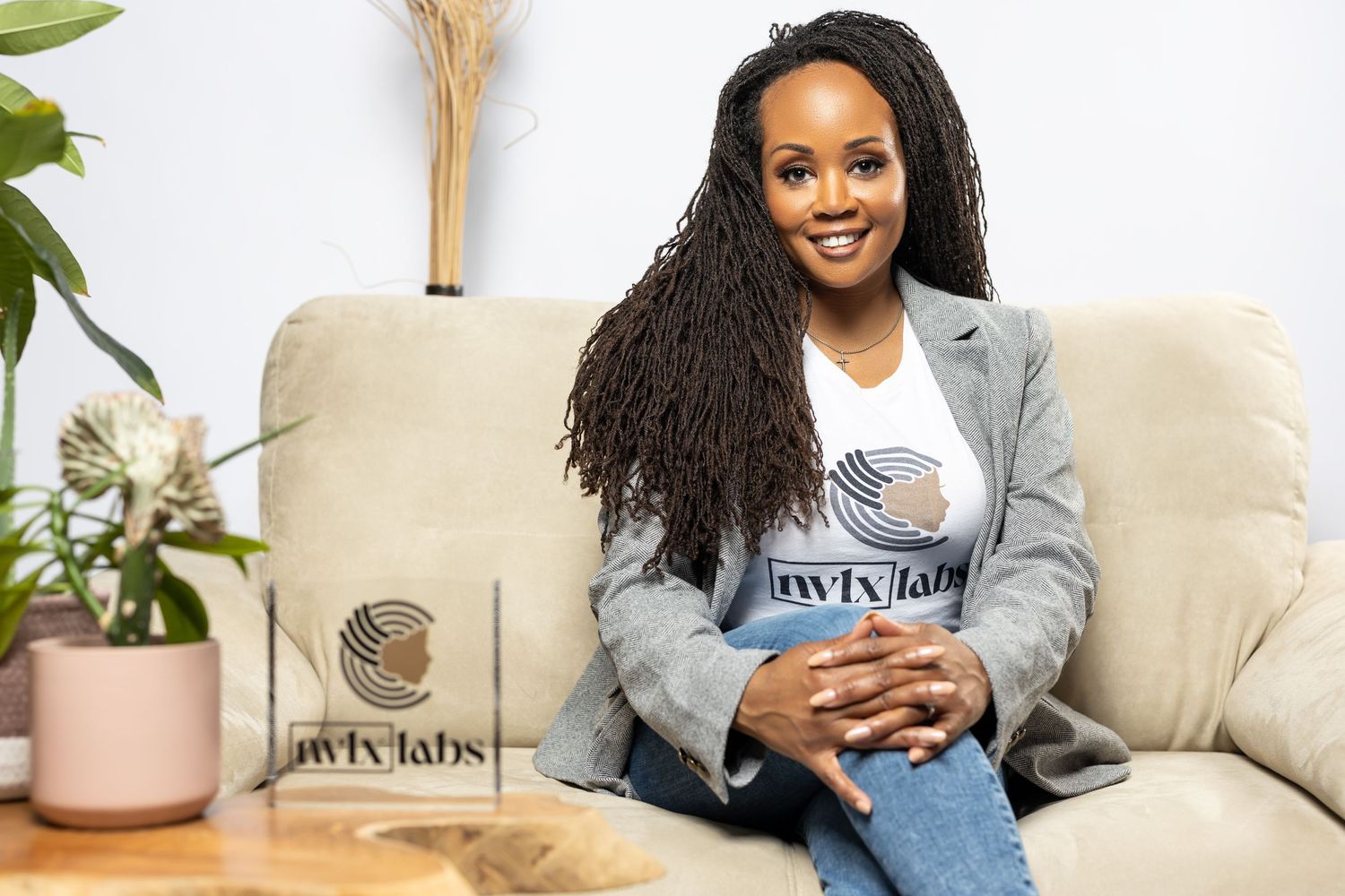 Casual portrait of woman in grey blazer sitting on couch with branded packaging.