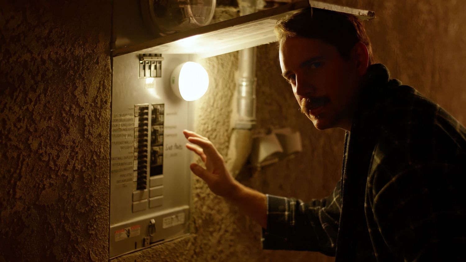 Person examining an electrical panel box in dim lighting.