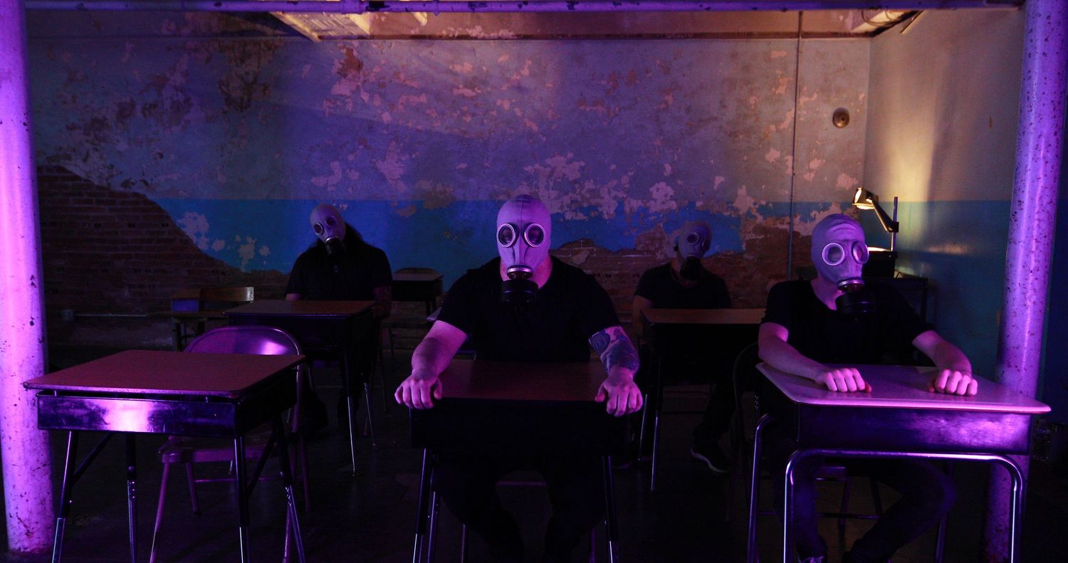 Three people wearing skull masks seated at tables under purple lighting in a dark room.