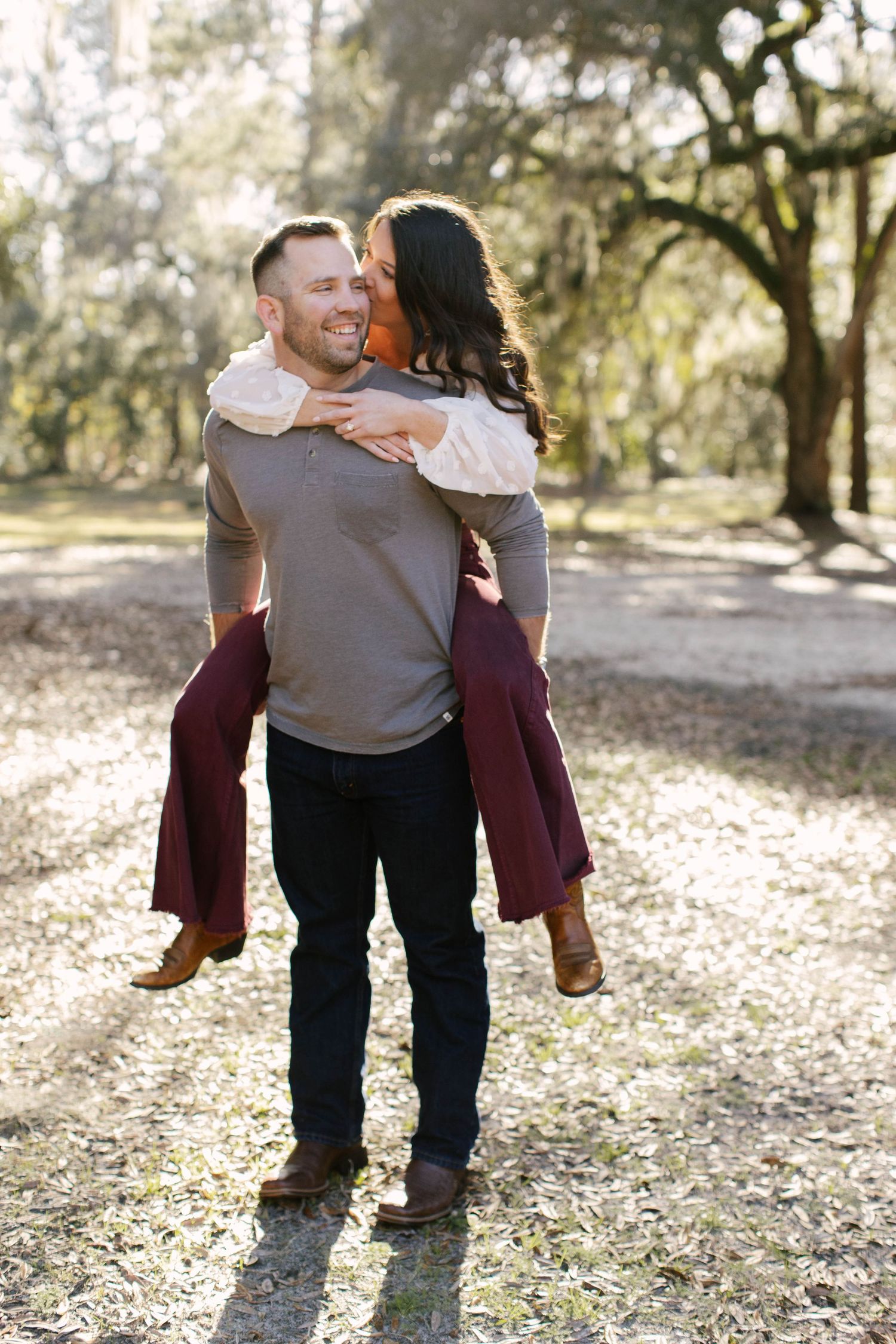 A romantic piggyback ride moment in a sun-dappled forest setting.