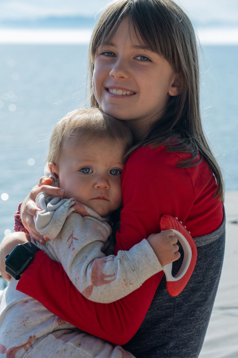 Tender moment captured between parent and child against bright waterfront backdrop.