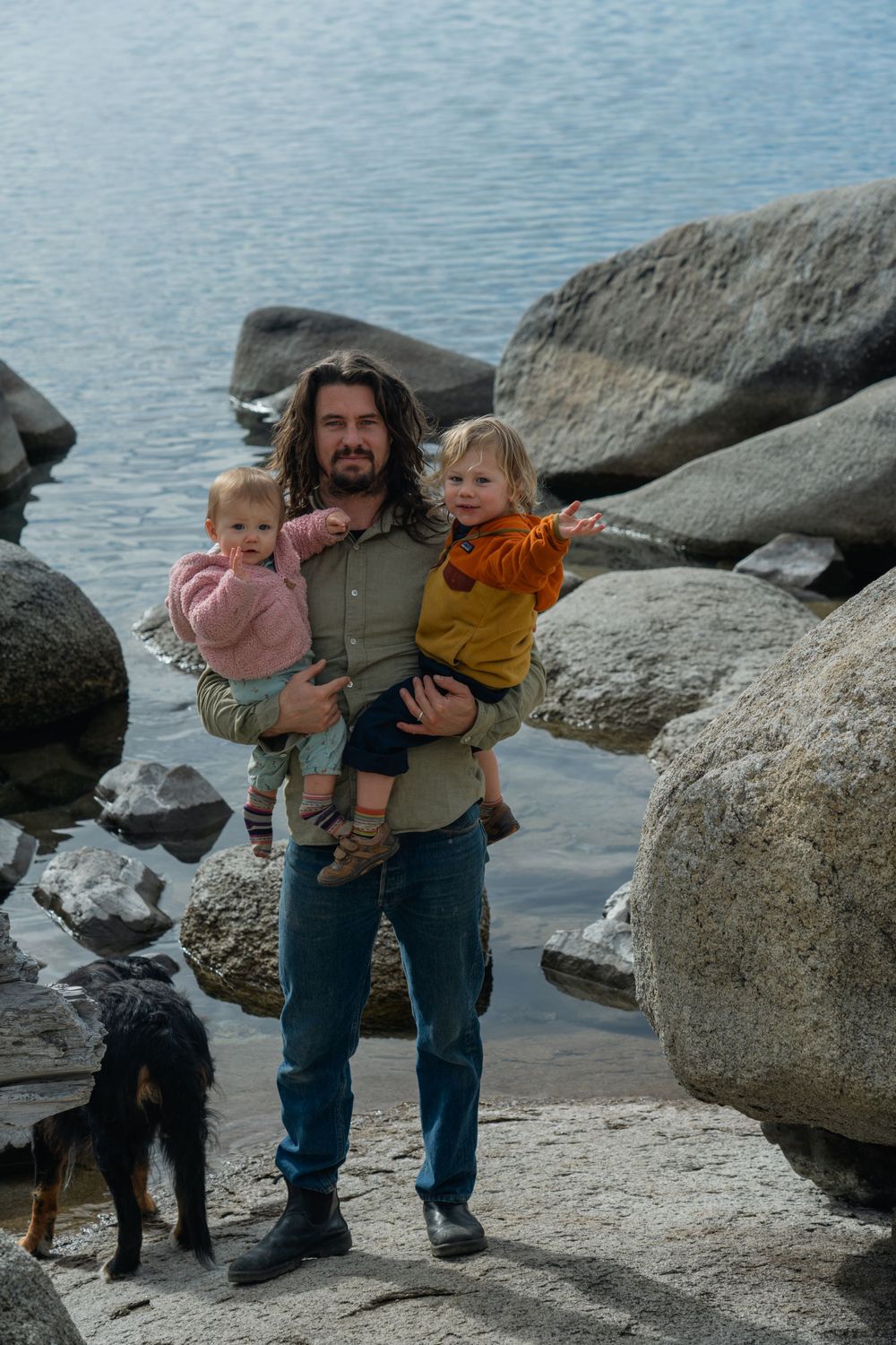 Family photography enjoying time together on rocky beach of East Shore Lake Tahoe Nevada with their black dog near the water.