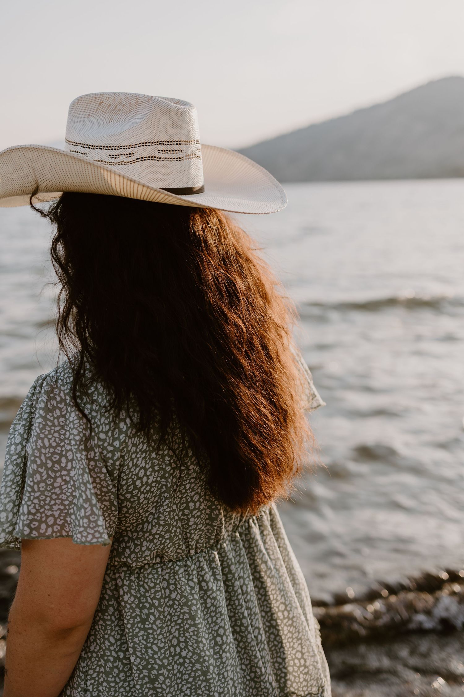 Side view of person in floral dress and white cowboy hat looking at ocean view.