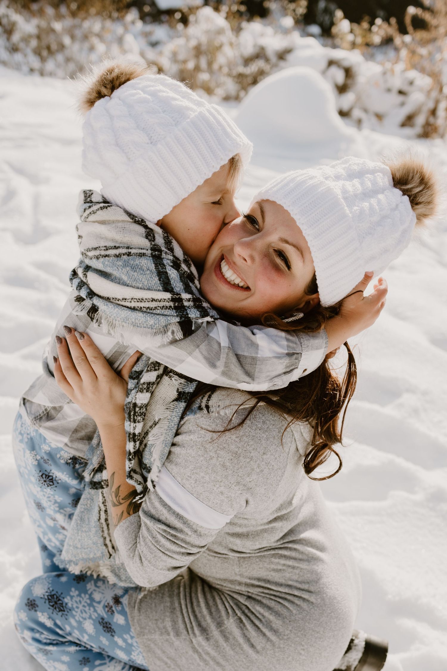 Joyful winter moment between two people wearing matching white pom beanies in the snow.