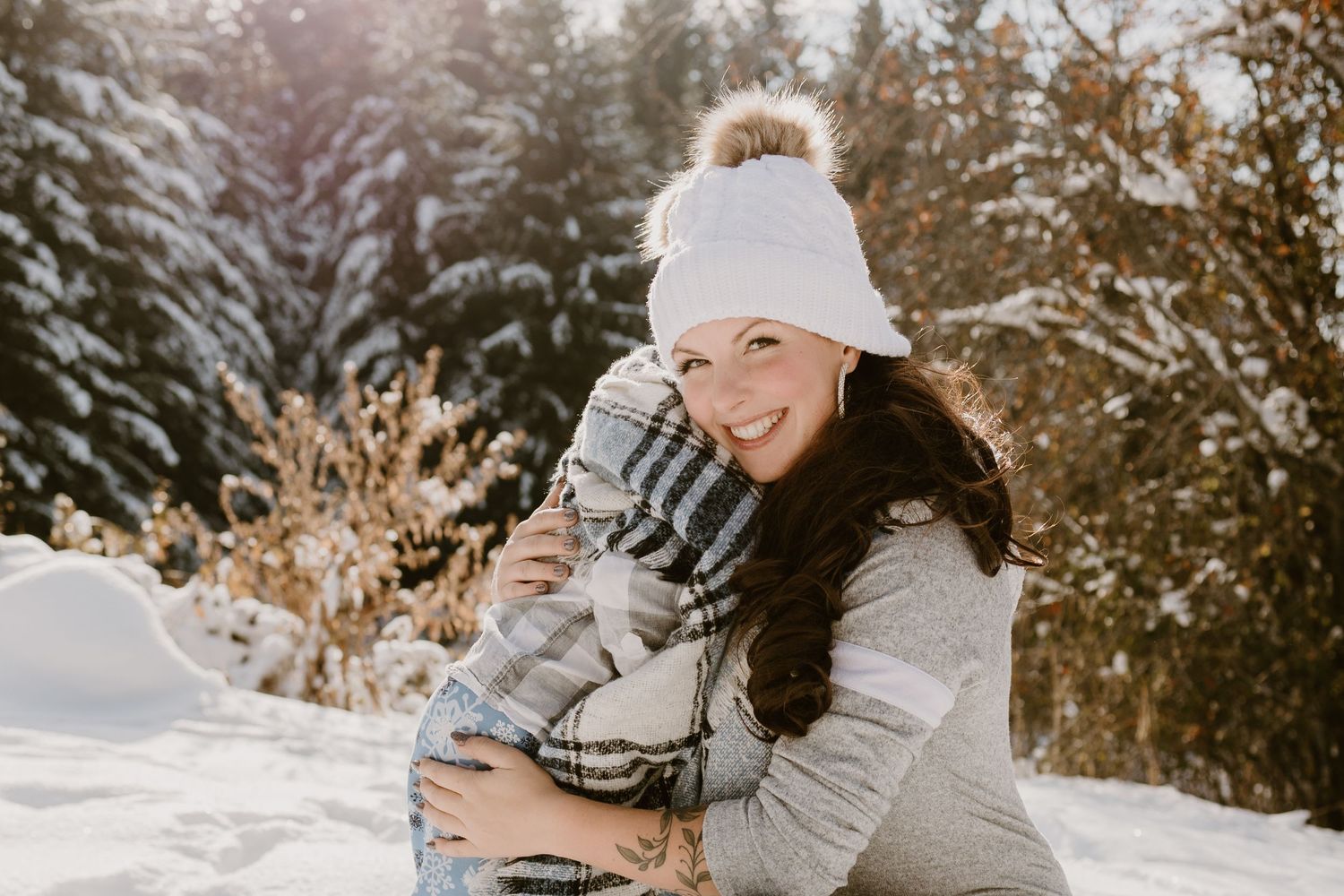 Heartwarming winter scene with two people in matching white pom beanies embracing in snow.