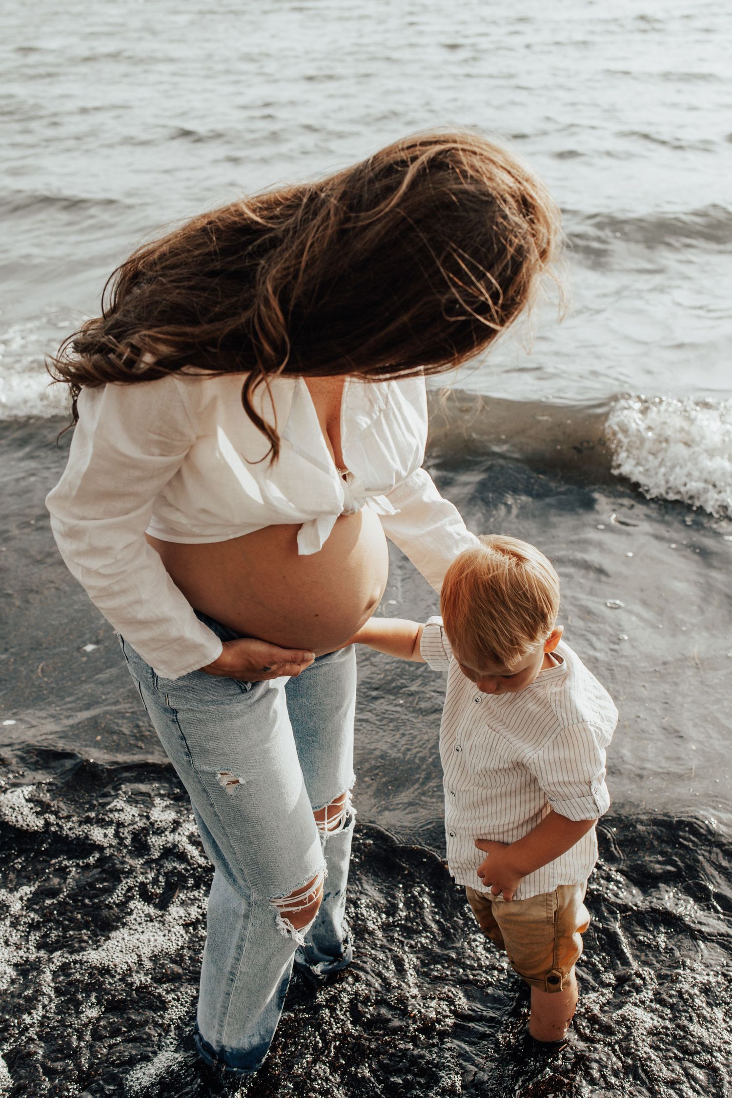 Mother and toddler explore rocky beach together near ocean waves.