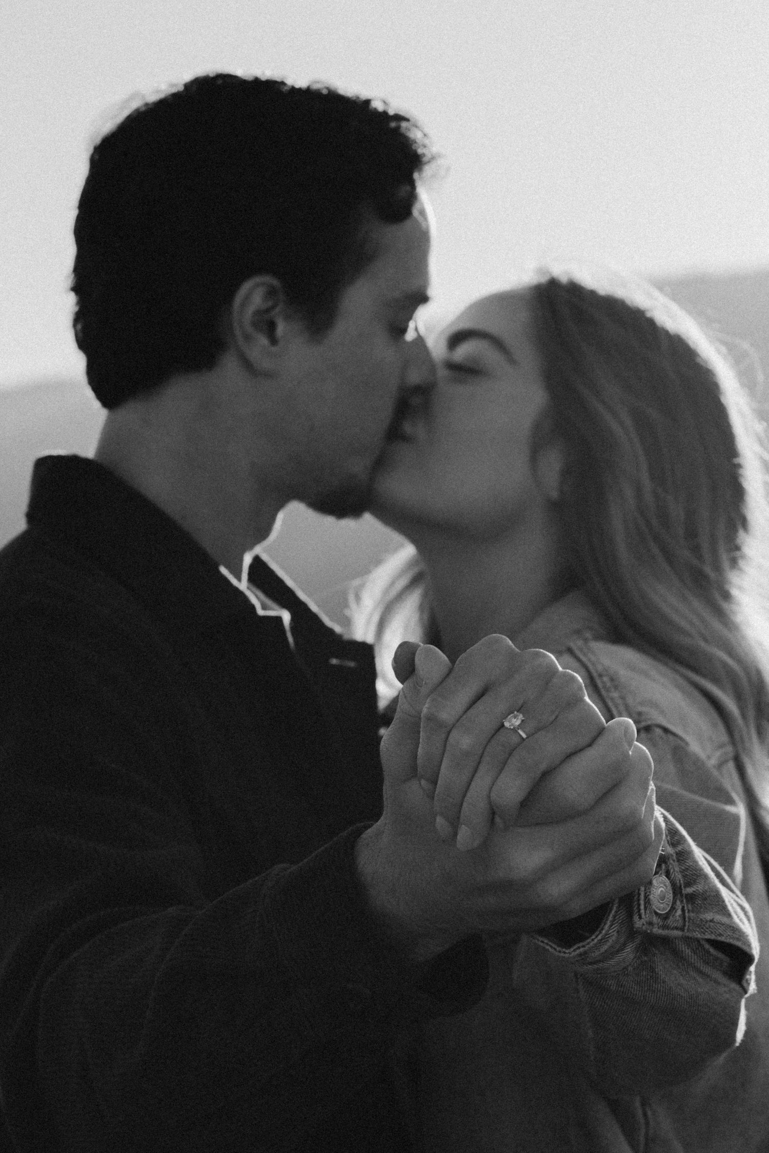 Black and white photo of couple dancing and holding hands with mountains in background.