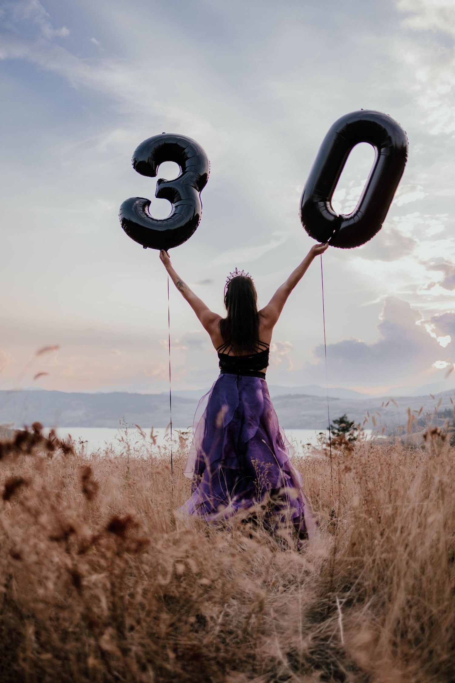 Person holding up number 30 balloons in a field at sunset against mountain backdrop.