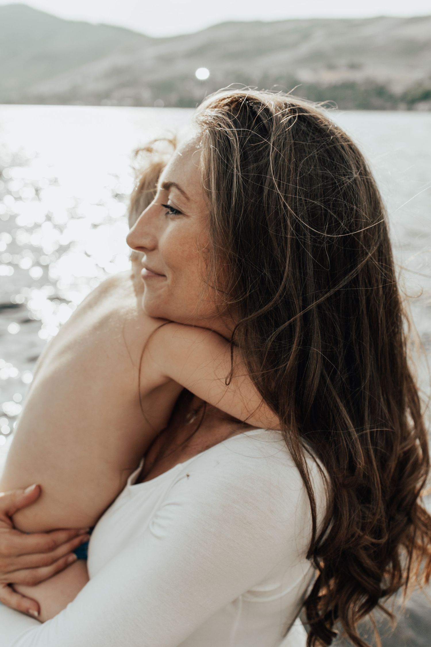 Profile portrait of woman with flowing hair against sparkling water and mountain backdrop.