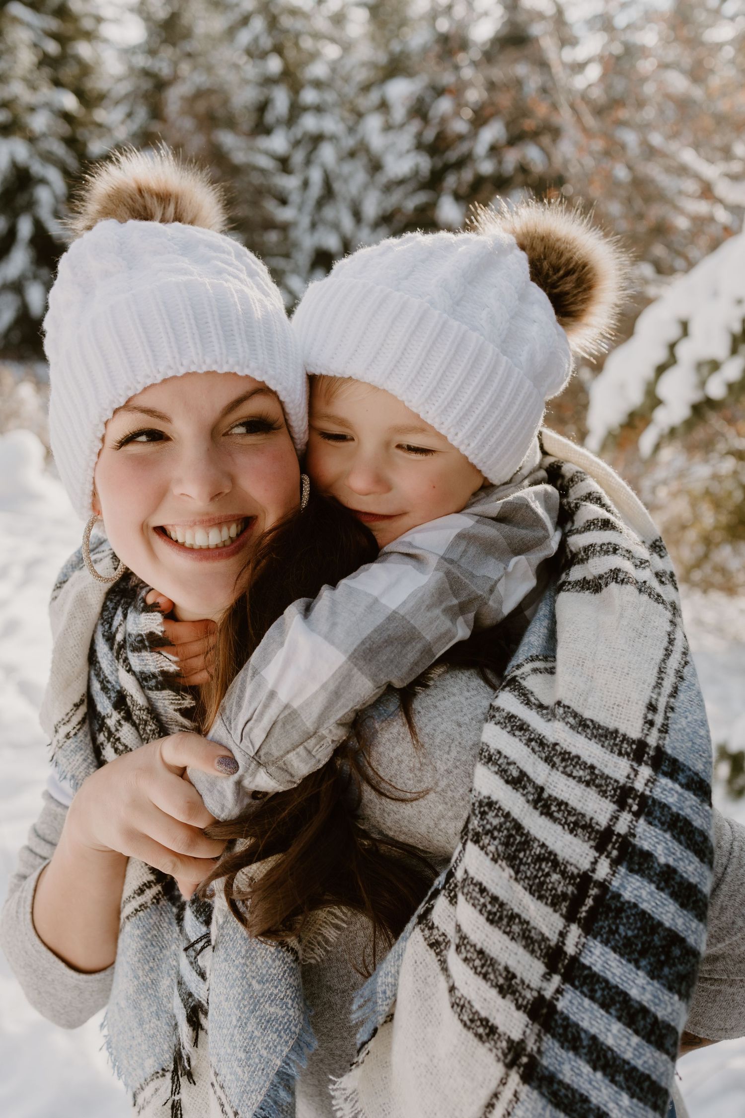 Winter portrait of pair wearing matching white knit beanies and plaid scarves in snowy setting.
