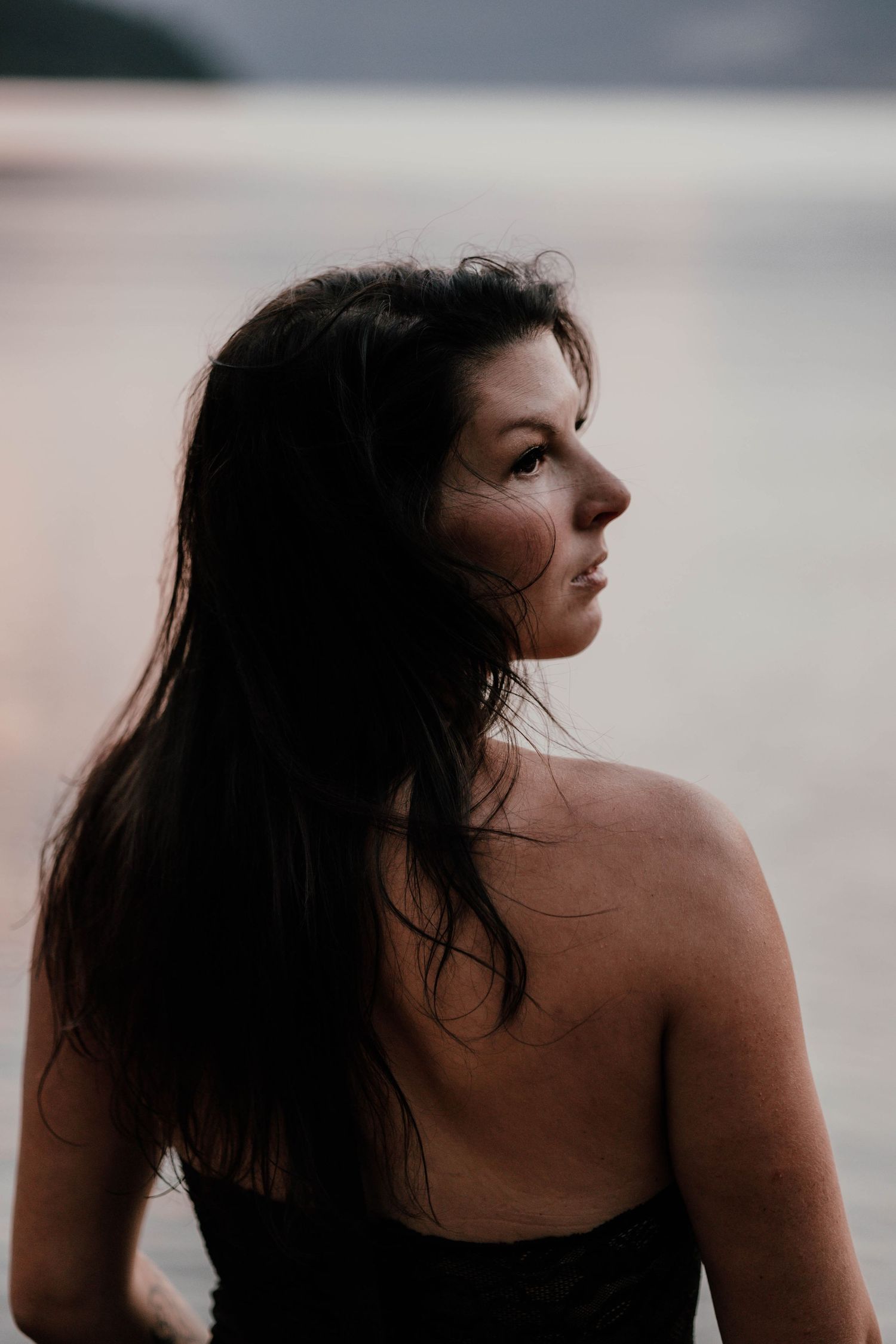 Side profile portrait of person with long dark hair against blurred sunset background.