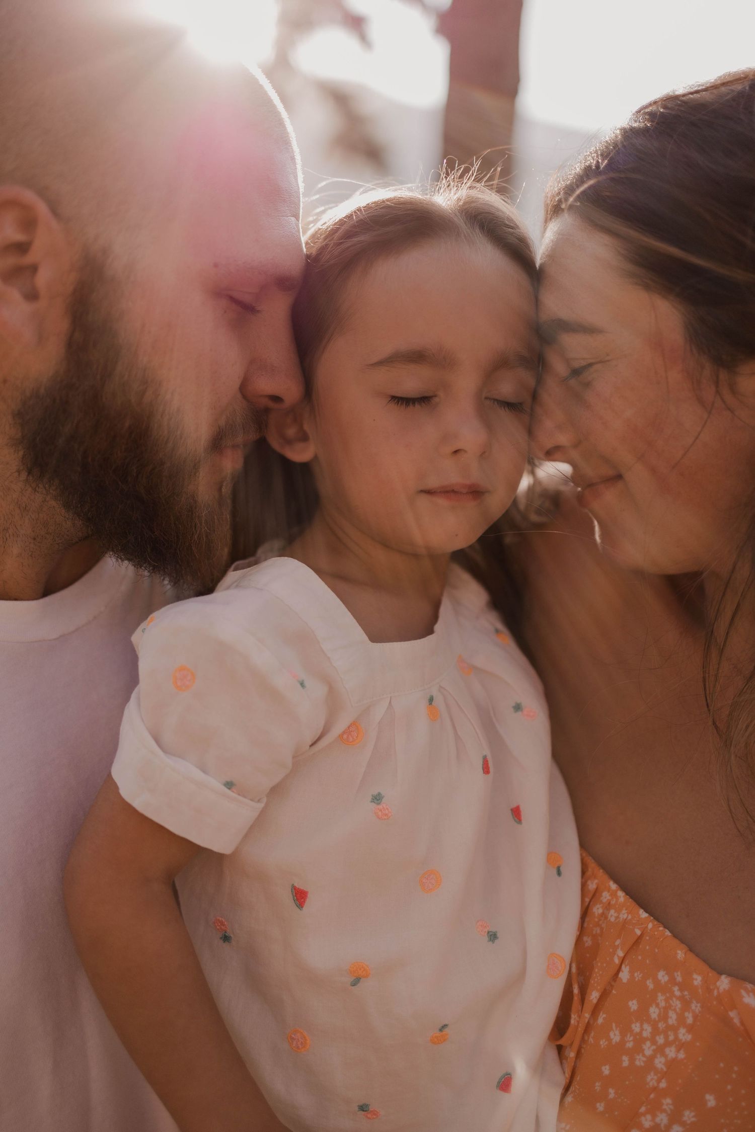 Intimate family portrait with warm sunlight and soft expressions.