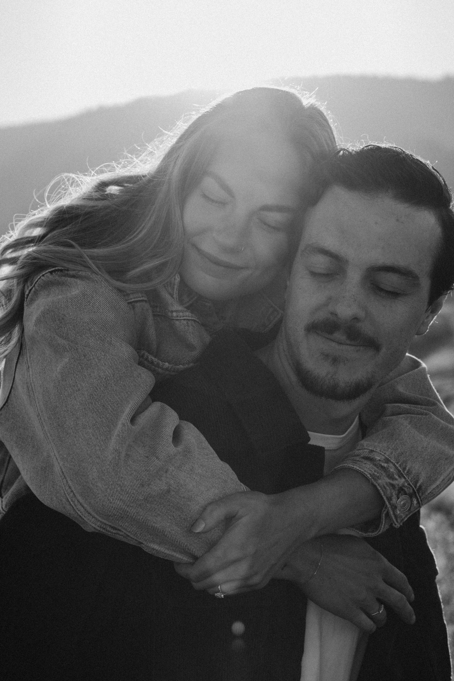 Couple sharing tender embrace outdoors with backlit sunlight creating romantic atmosphere.