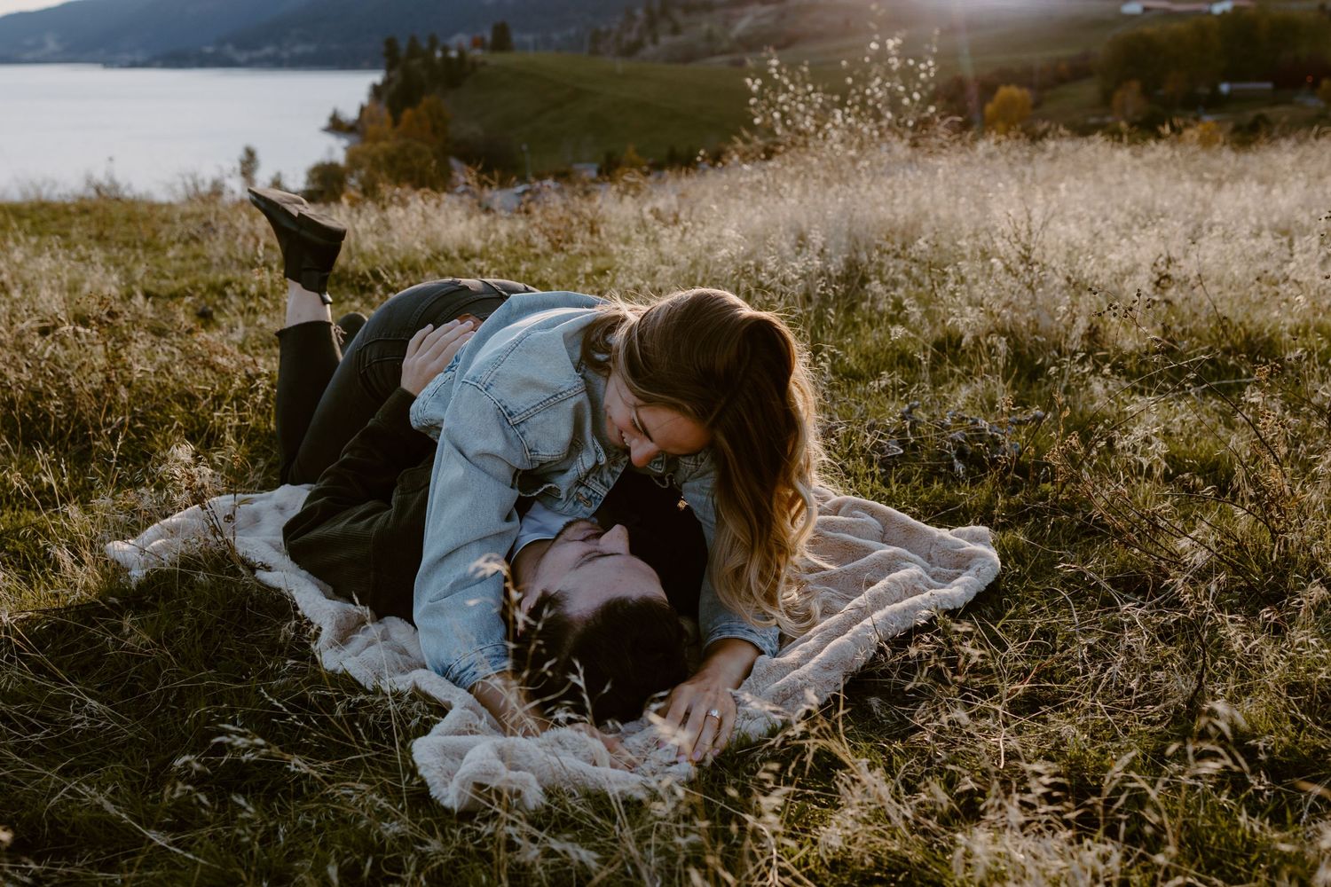 Person lying on blanket in scenic mountain meadow with lake view at sunset.