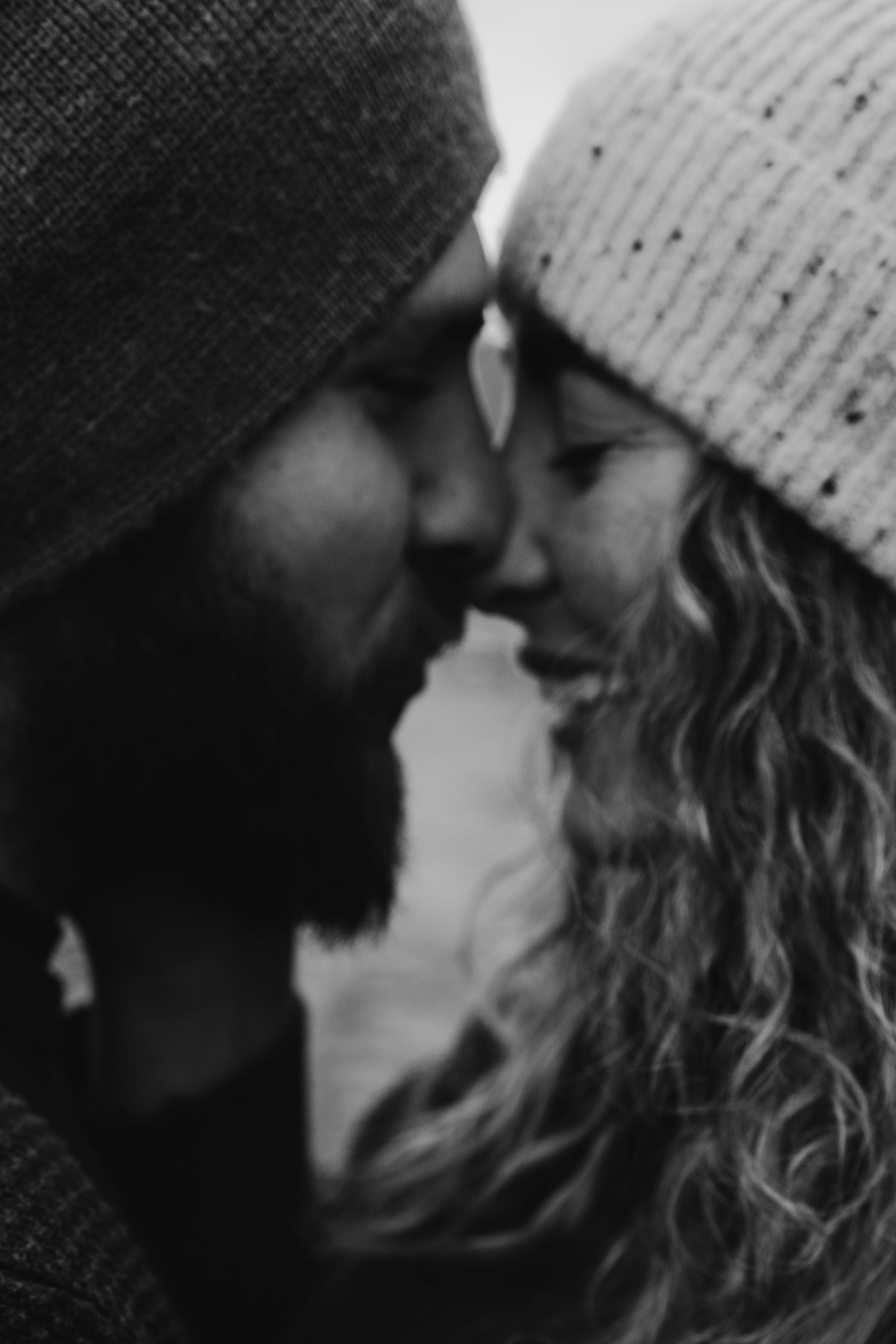 Intimate black and white portrait of couple in winter beanies with foreheads touching.