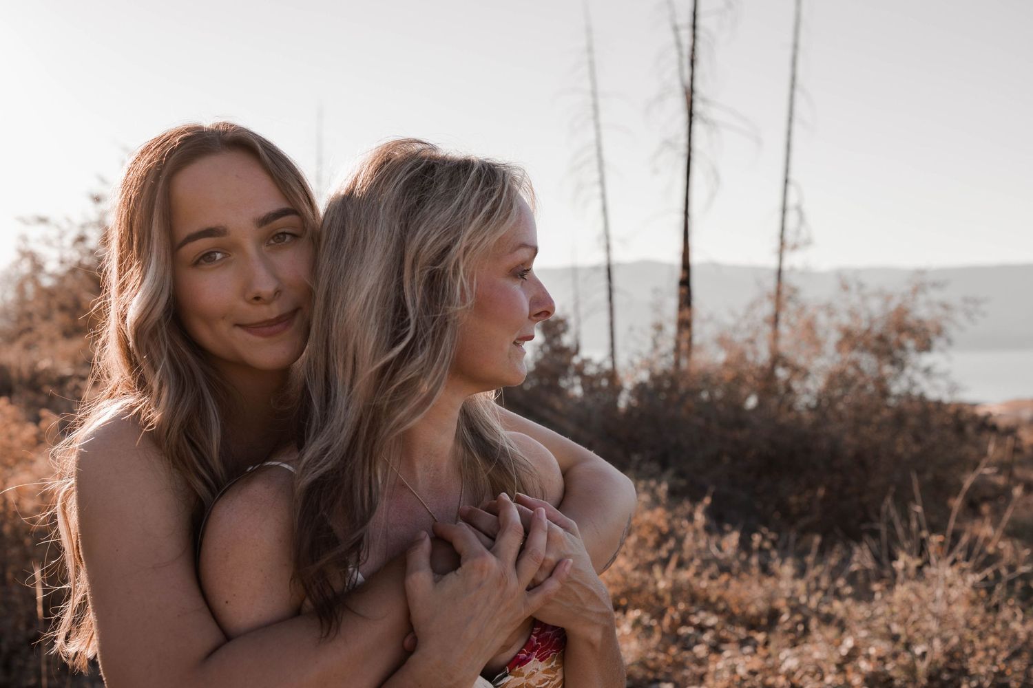 Two friends sharing an intimate moment embracing outdoors with golden sunlight.