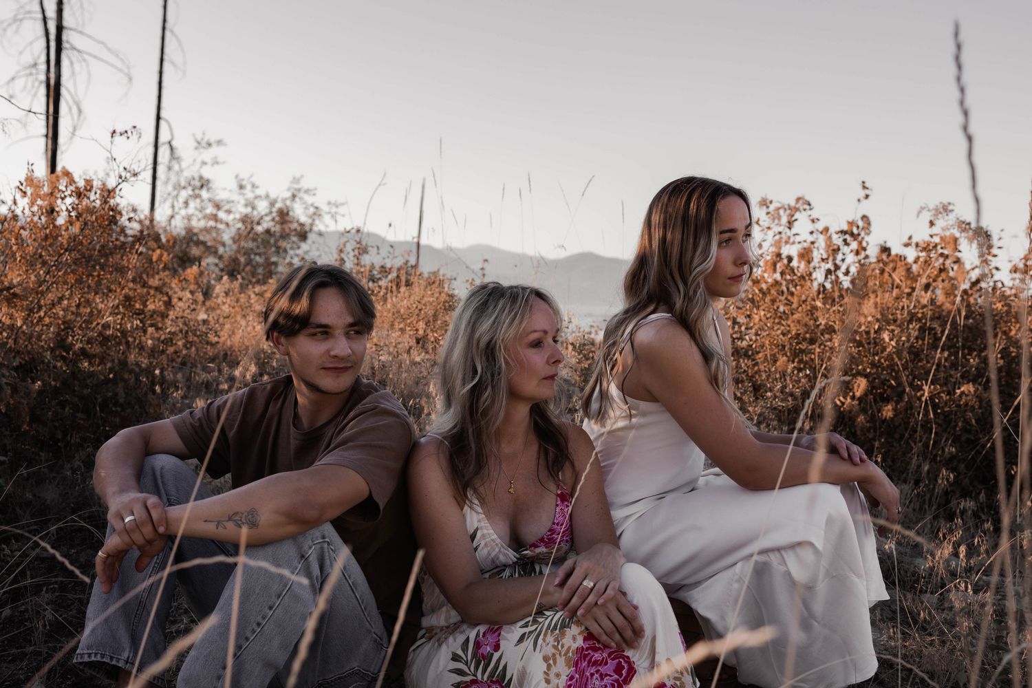 Three friends relax outdoors at sunset surrounded by autumn foliage and mountain views.