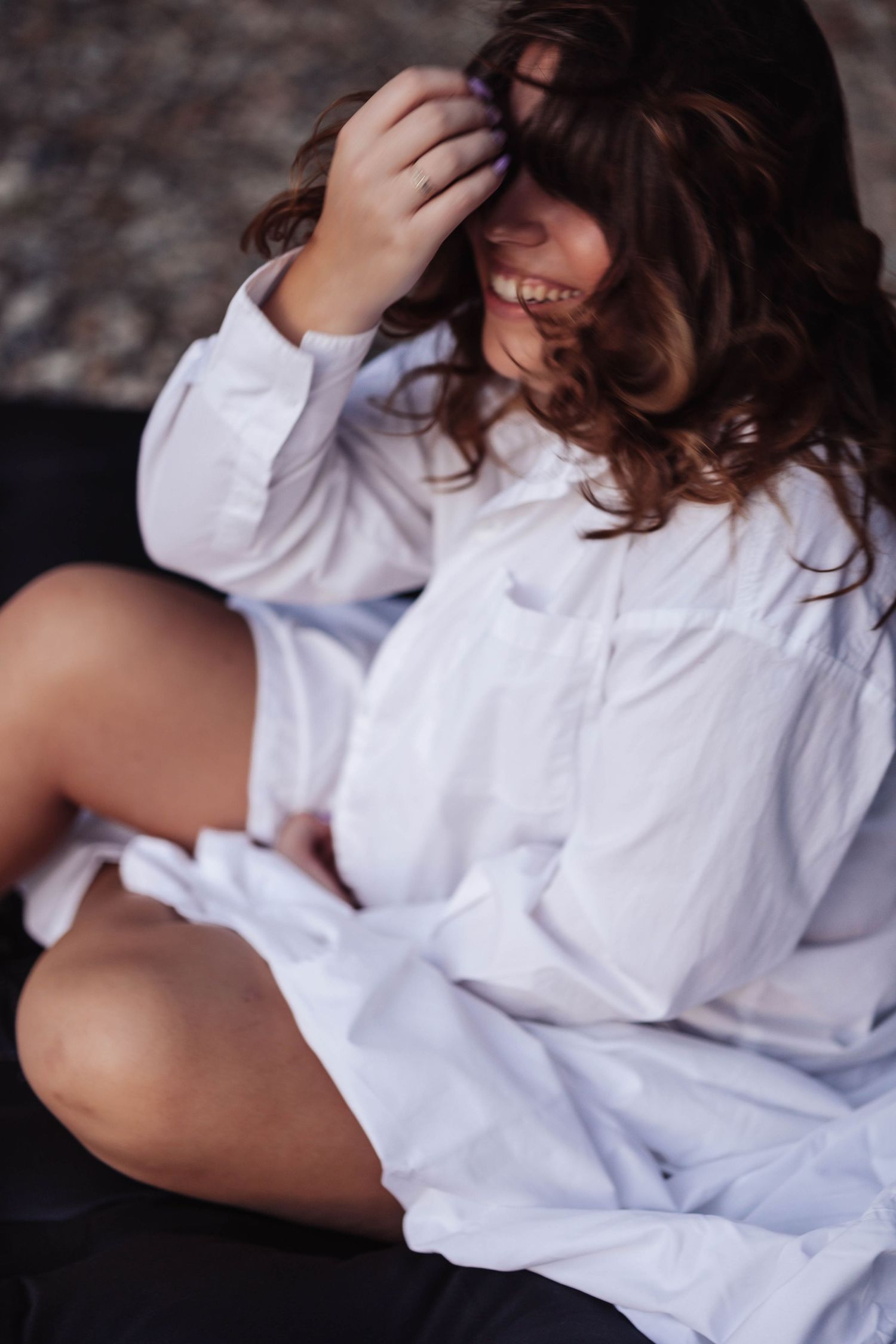 Person in oversized white button down shirt sitting casually with relaxed expression.
