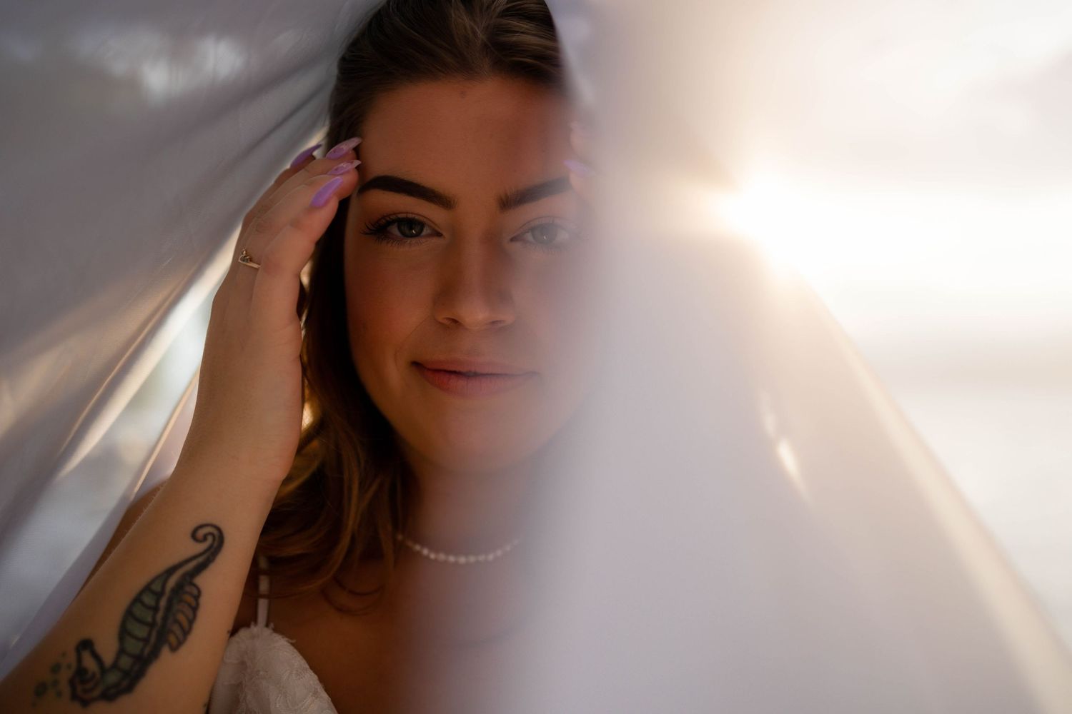 Ethereal bridal portrait with soft light filtering through veil showing tattoo detail.