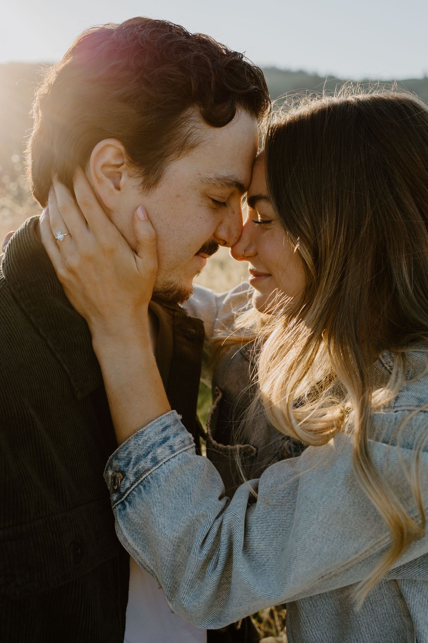 Romantic couple sharing an intimate moment in golden sunlight while wearing casual denim clothing.