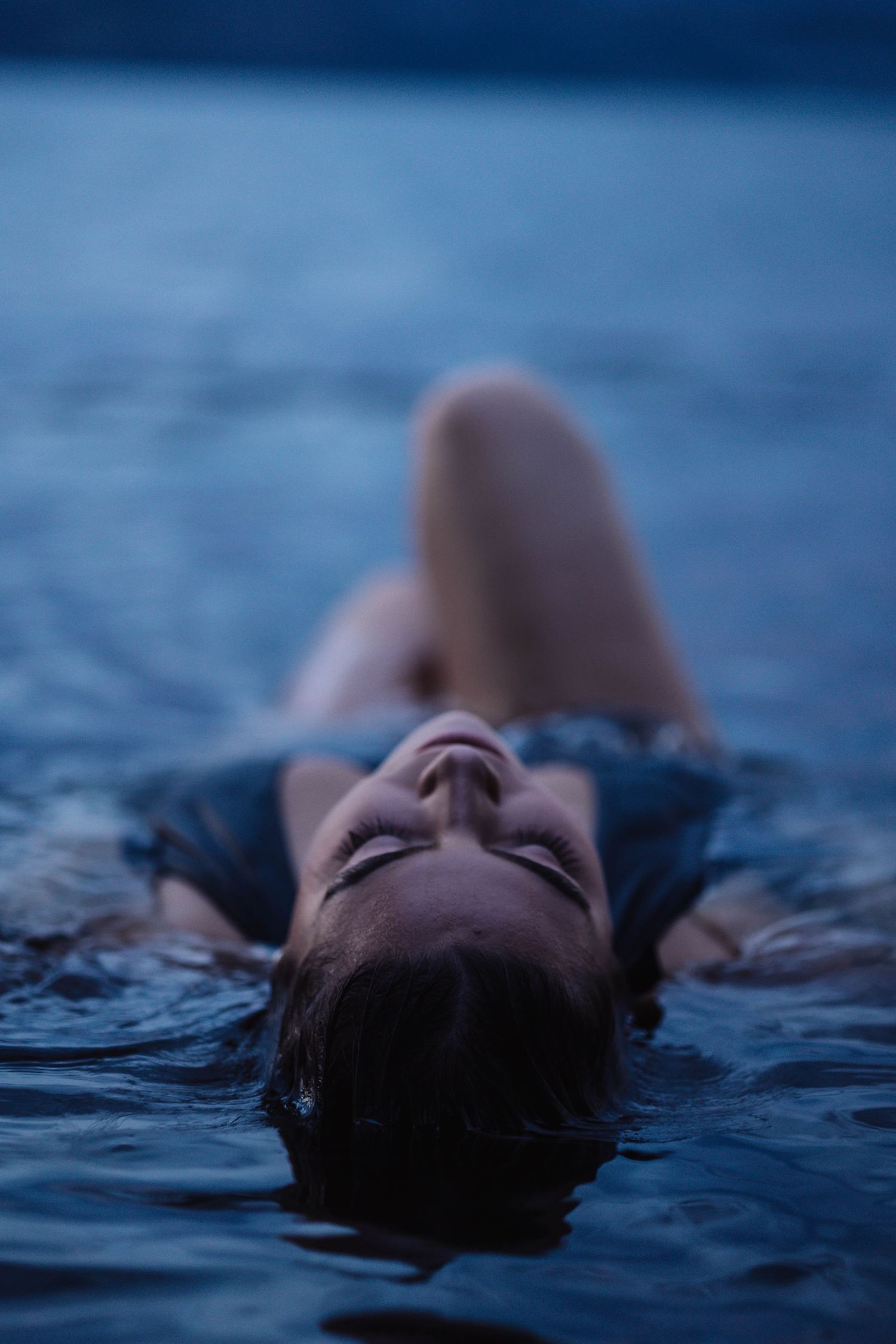 Figure floating peacefully in dark blue water during twilight hours.