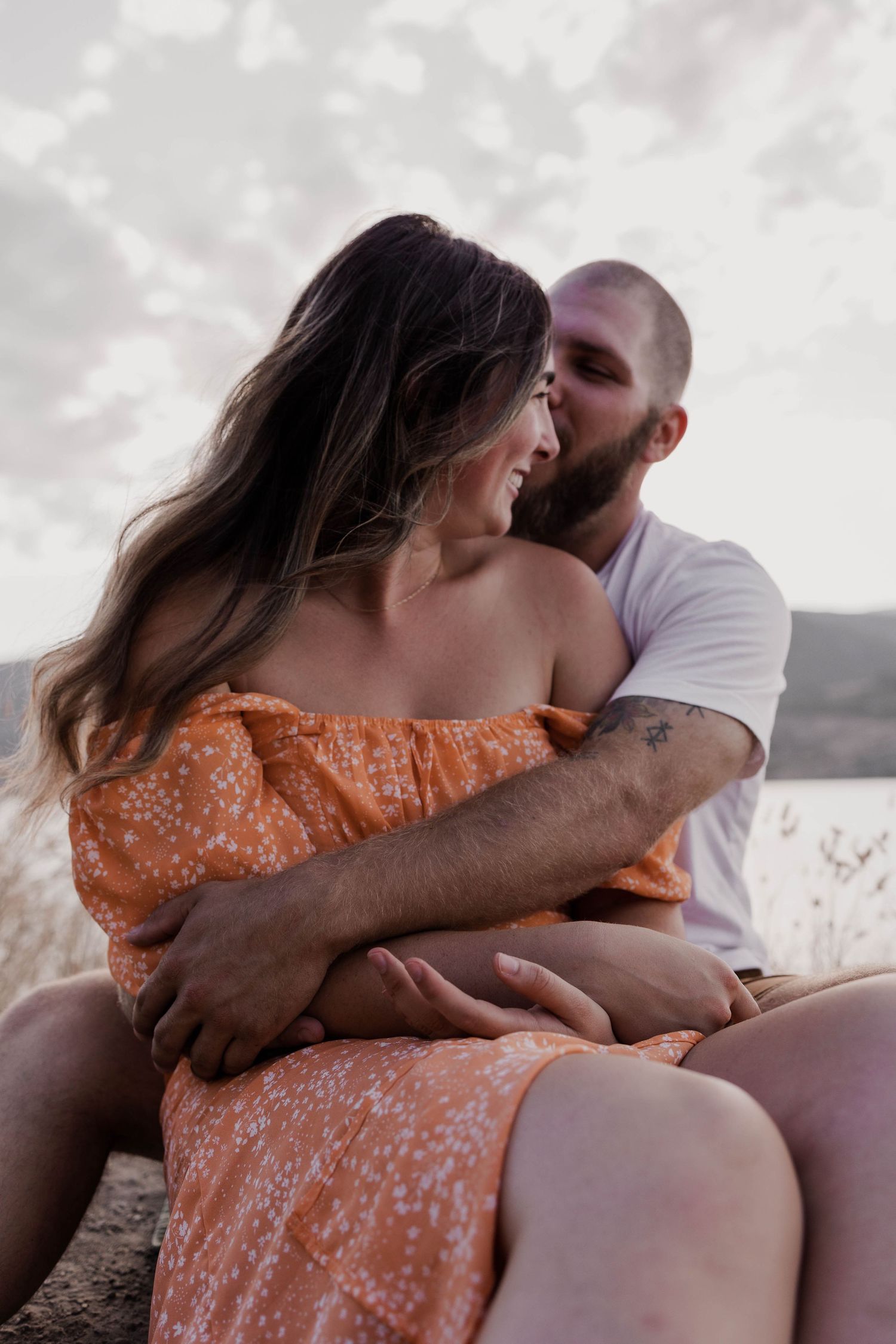 Romantic couple embracing on rocky outcrop at sunset.