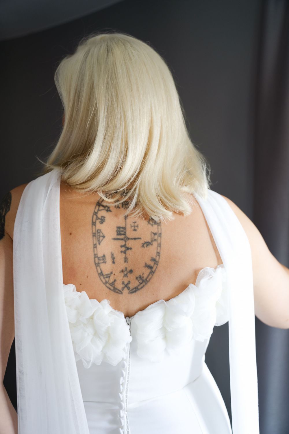 Back view of a wedding dress showing intricate button details and a tattoo design.
