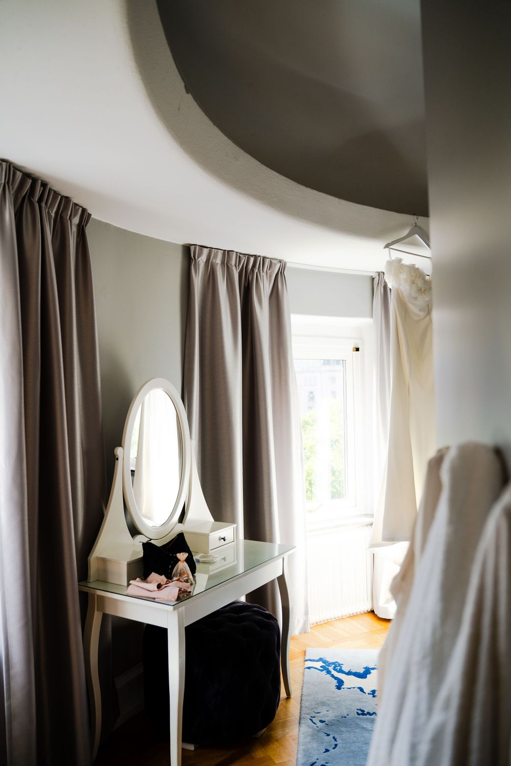 A minimalist dressing room with white vanity, oval mirror and grey curtains.