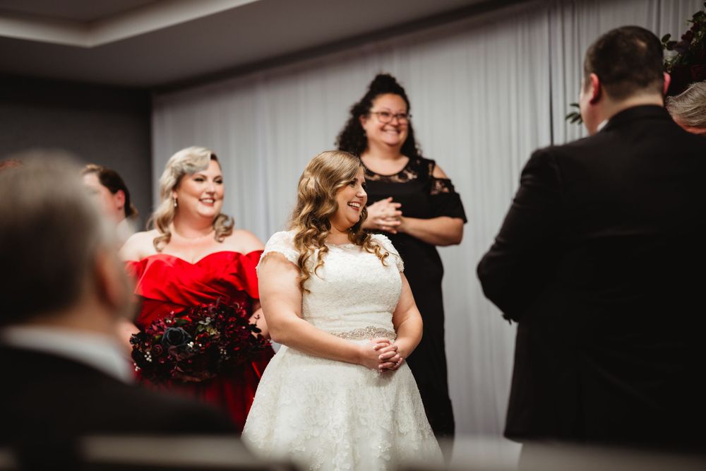Indoor wedding ceremony scene with bridesmaids in red dresses and white bridal gown.