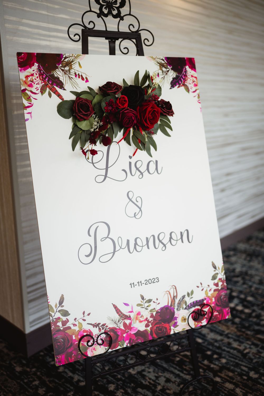 Wedding welcome sign with burgundy floral design displays names and date.
