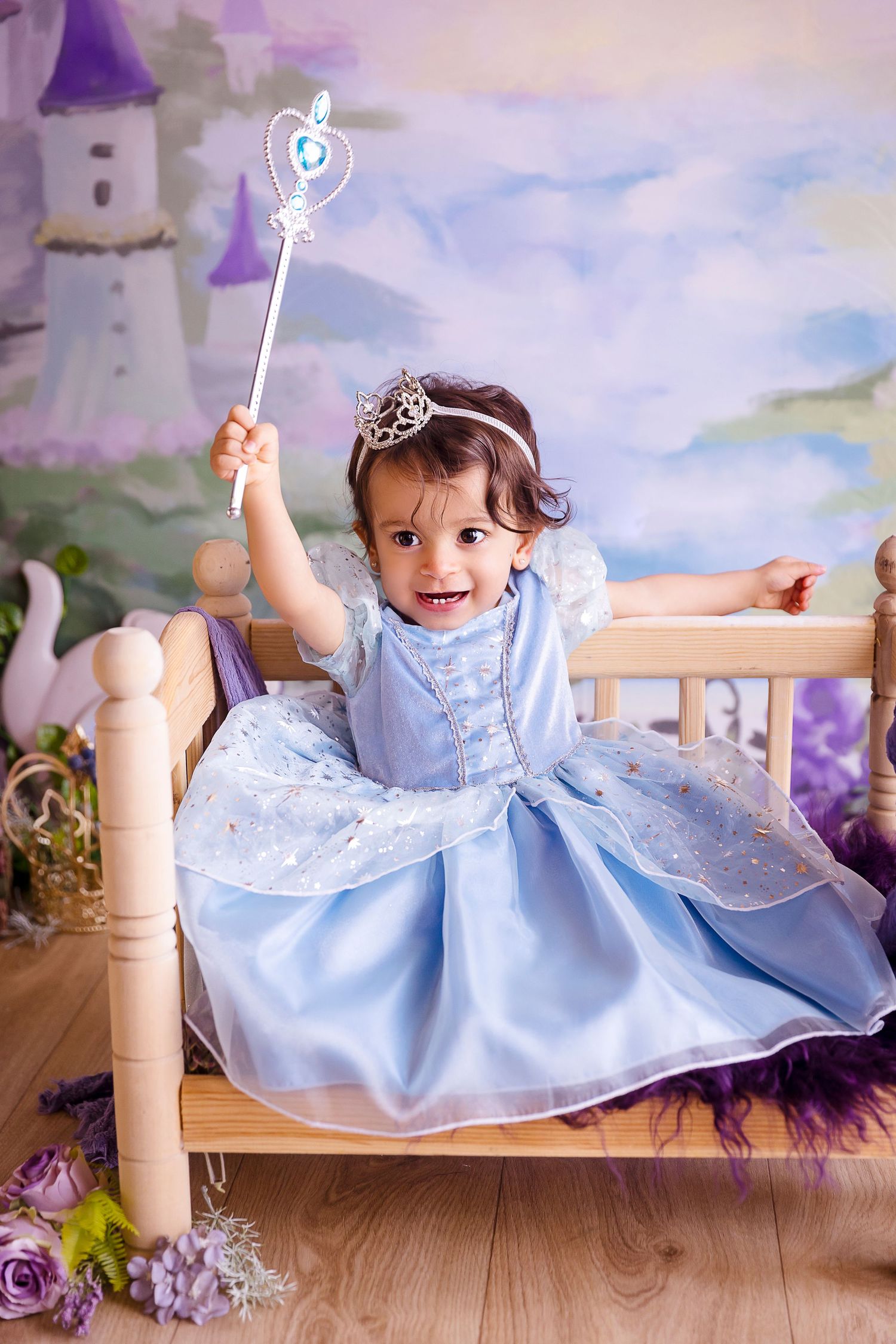 bebe contenta vestida de princesa con traje azul claro y brillo sentada en una camita de madera detres photography