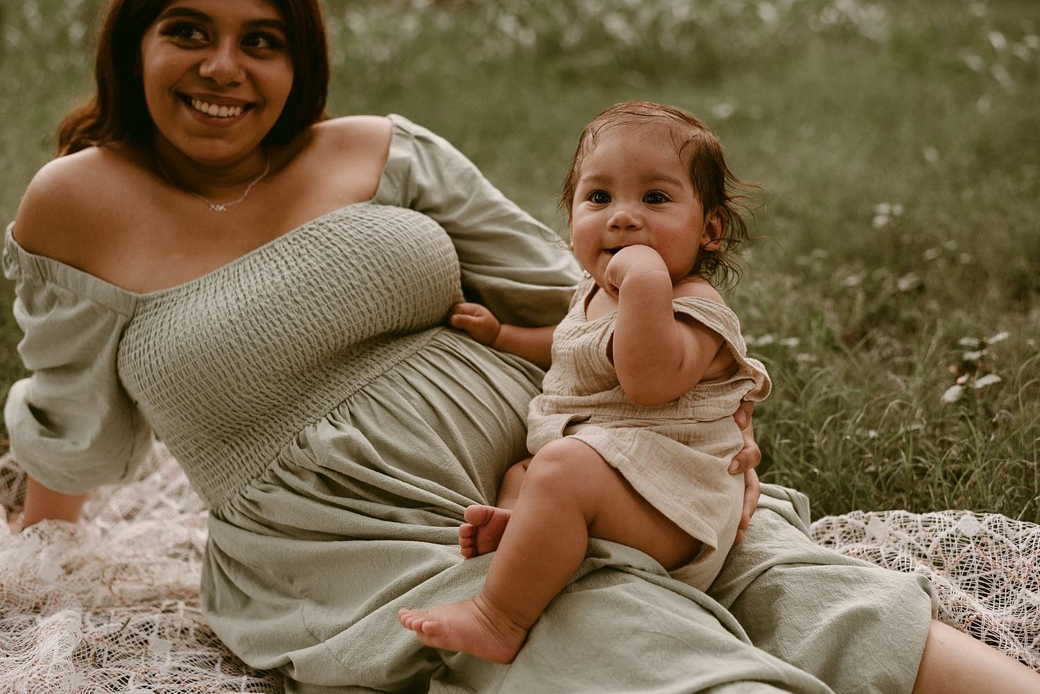 A candid moment captures parent and child laughing together on a lace blanket outdoors.