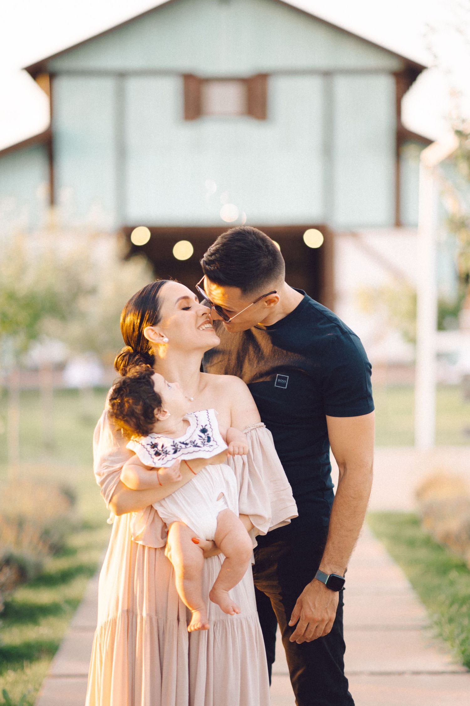 A tender family moment captured at sunset outside a rustic building with string lights.