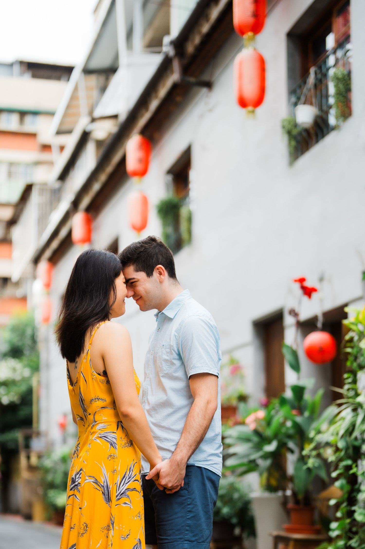 Romantic couple sharing intimate moment against wall with red lanterns and potted plants.