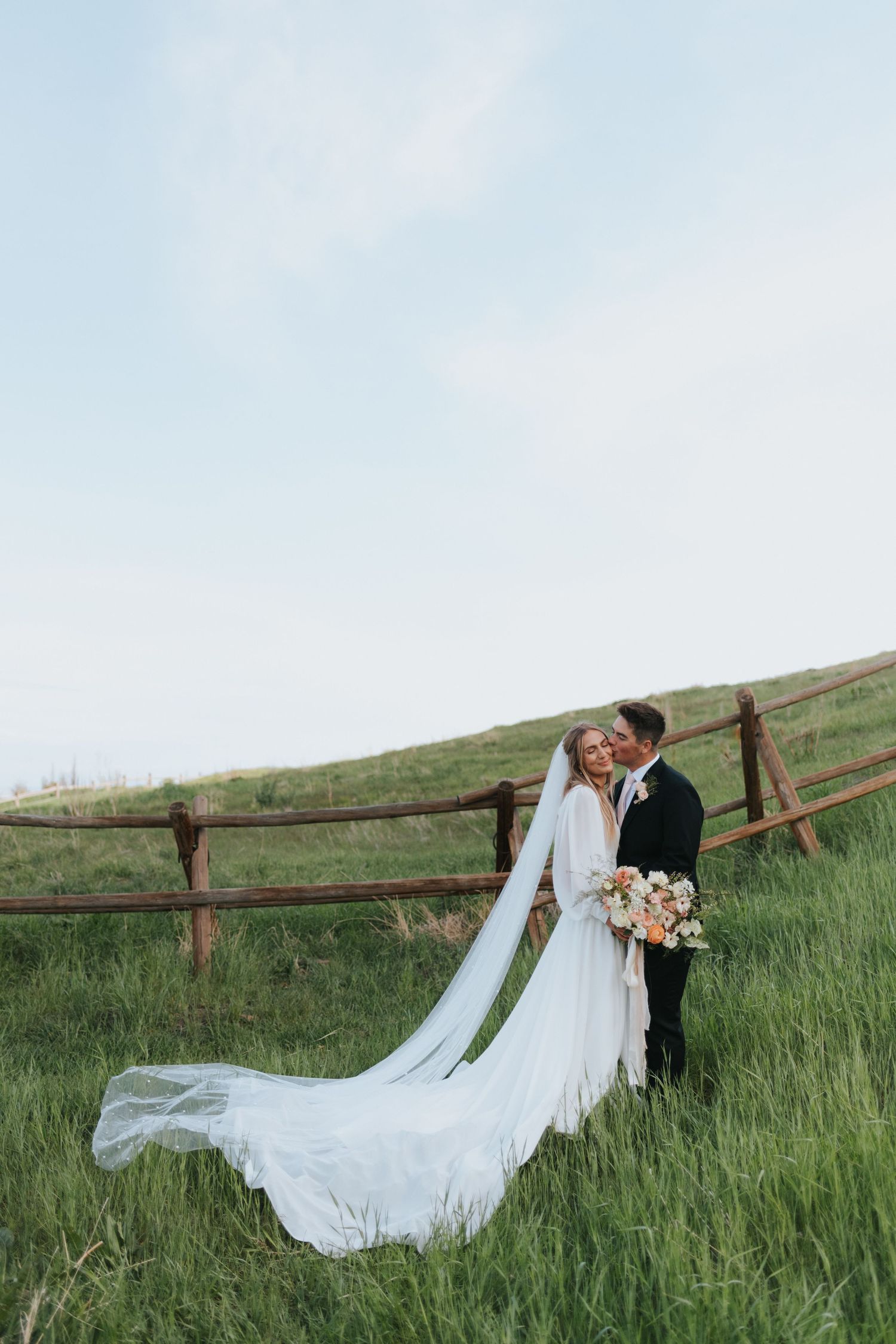 A couple embraces in rolling green hills near Bountiful Utah for their affordable wedding photographer.
