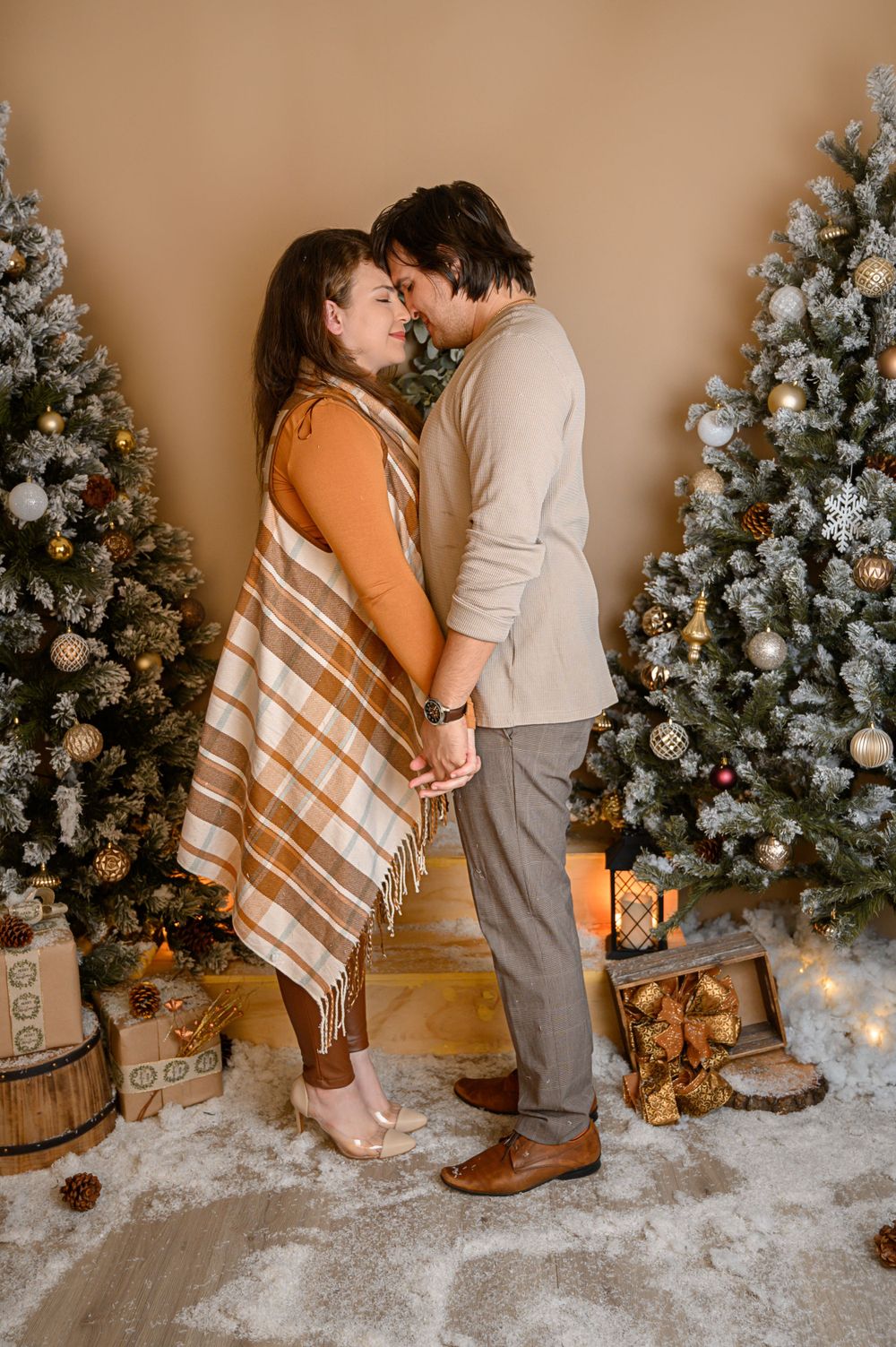 Intimate Christmas portrait session with couple sitting by decorated tree and faux snow setting.