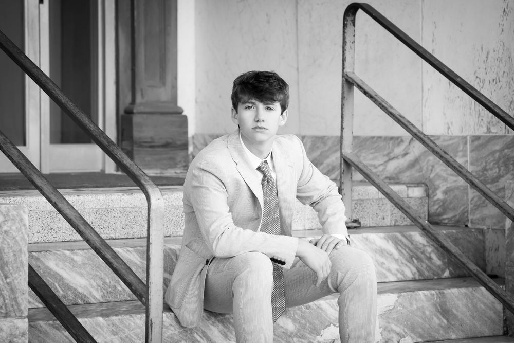 Black and white portrait of a person in a light colored suit sitting on concrete steps.