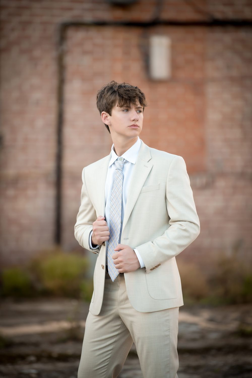 Portrait against brick wall featuring a person in cream colored suit with light blue tie.